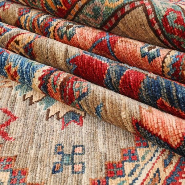 Stack of folded Kazakh rugs with typical Caucasian patterns in warm tones.