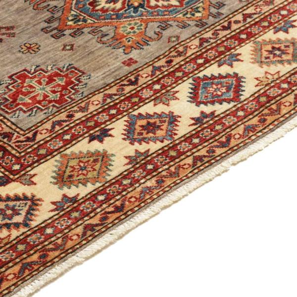 Detailed view of a hand-knotted Kazak rug with a geometric border pattern in red, blue, and beige.